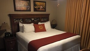 Habitación de hotel con una cama grande, una mesita de noche con lámpara, una silla y dos cuadros en la pared.