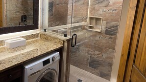 Un baño moderno con ducha de vidrio, lavamanos integrado y lavadora.