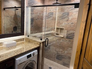 A modern bathroom with a glass-enclosed shower, a built-in sink, and a washing machine. - Cozy 2-bedroom cabin in gorgeous Gatlinburg with AC. Mountain View. Balcony  (Gatlinburg)