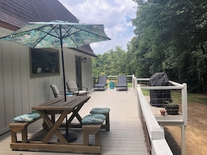 Una terraza de madera con mesa y sillas, una sombrilla y una zona de barbacoa.