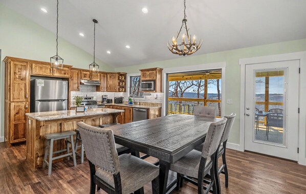 A kitchen with wooden cabinets, stainless steel appliances, a dining table with chairs, and a large window with a view.