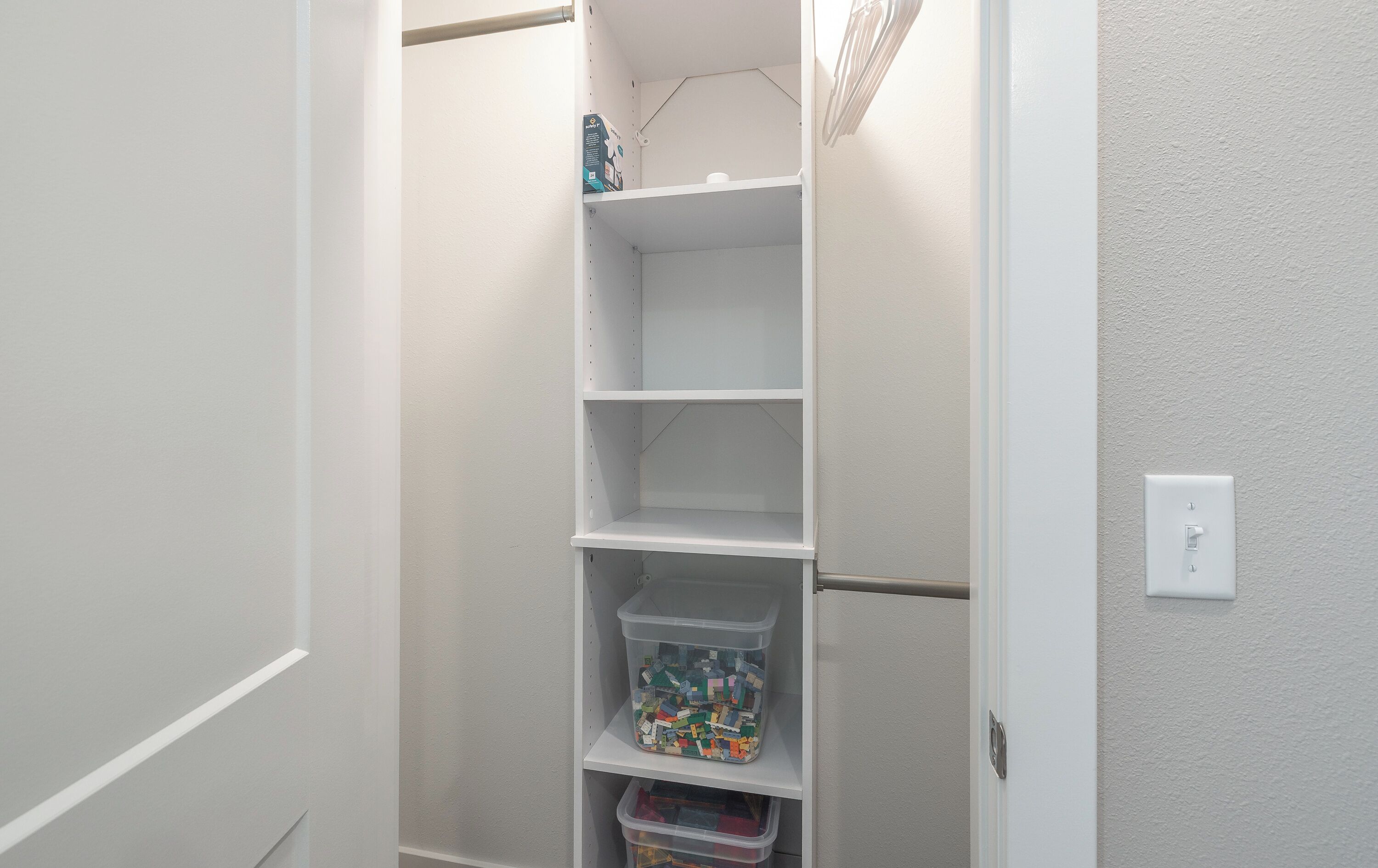 A white closet with shelves and a hanging rod, containing storage bins and a small item on the top shelf.