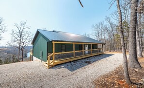 A cabin with a porch, a stone foundation, and a view of the surrounding forest.