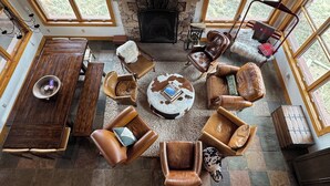 Un salón amplio con chimenea de piedra, mobiliario de cuero y ventanas grandes.