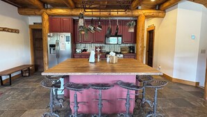 Una cocina amplia con una isla grande, taburetes rojos tipo bar y ollas colgantes.