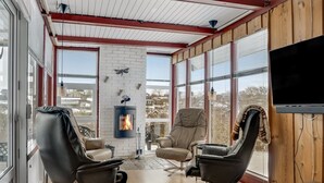 Ein gemütliches Wohnzimmer mit Kamin, Ledersesseln, Fernseher und großen Fenstern.