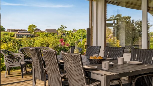 Eine Terrassengrundstück mit Korbstühlen und einem Tisch, mit Blick auf einen Garten und Häuser.