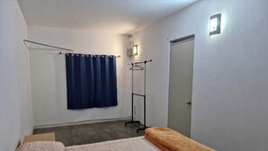 Ein Zimmer mit einem Bett, einem blauen Vorhang, einem Kleiderhaken und einer Tür.