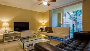 Una sala de estar con un sofá, una mesa de centro de vidrio, un televisor sobre un mueble bajo y un balcón con vistas.