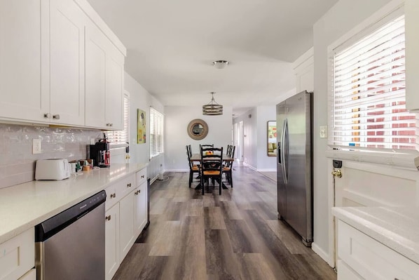 A modern kitchen with white cabinets, a dishwasher, and a dining area with a table and chairs. - Renovated House 9 Miles from Downtown ATL, Great Backyard on a Cul-de-sac! (Atlanta)