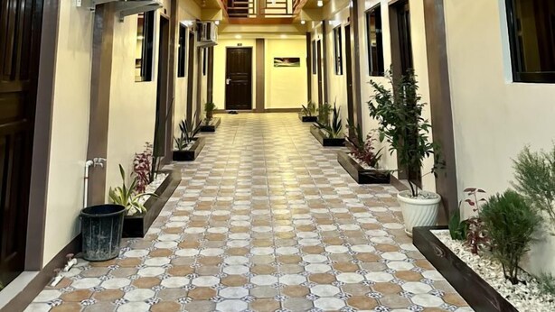 Un pasillo de hotel con tragaluz, barandillas de madera, plantas en macetas y suelo de baldosas.
