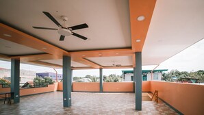 Eine offene Terrasse mit Deckenventilatoren, orangefarbenen Wänden und ein gefliestem Boden.