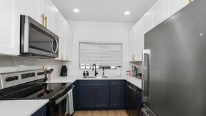 A modern kitchen with white cabinets, a stainless steel refrigerator, a built-in oven, and a microwave.