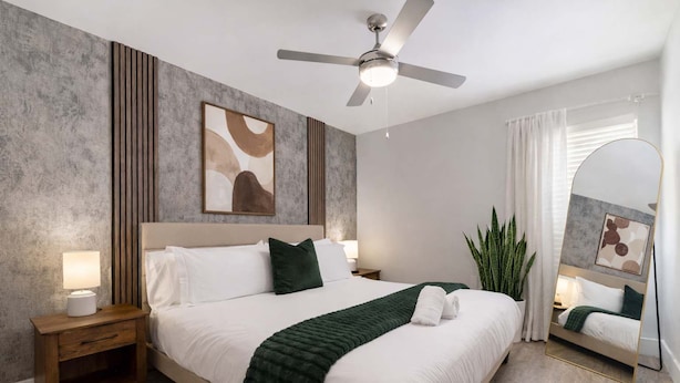 A modern hotel room with a large bed, a ceiling fan, a bedside table with a lamp, a mirror, and a potted plant. - Chic South Tampa Retreat  2 King Beds  Pool, Gym & Prime Walkable Location (Tampa)