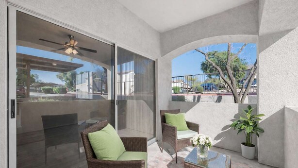 Un patio techado con puertas corredizas de vidrio, mobiliario de mimbre, ventilador de techo y una planta en maceta.