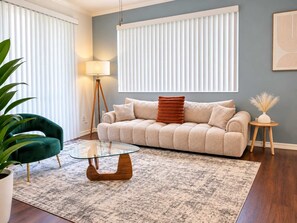 Ein Wohnzimmer mit einer Couch, einem Glastisch, einer Lampe und einem Blumentopf.