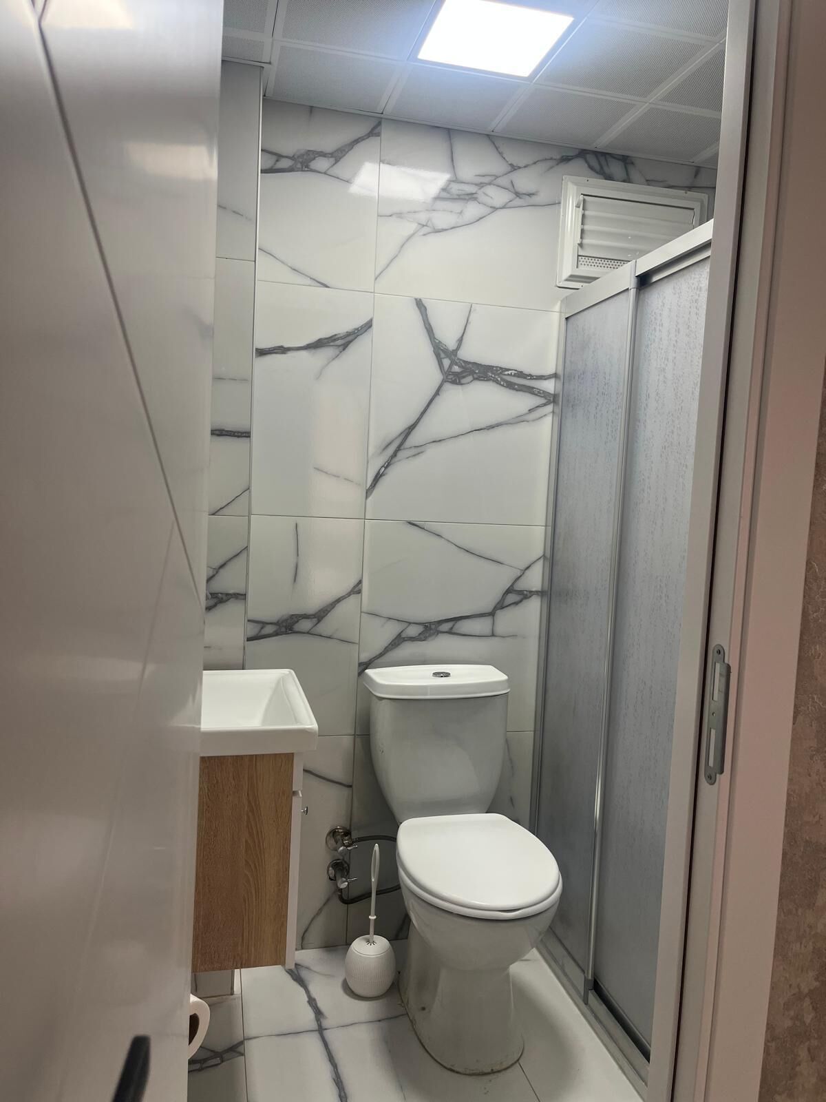 A bathroom with marble tiles, a toilet, a sink, and a shower.
