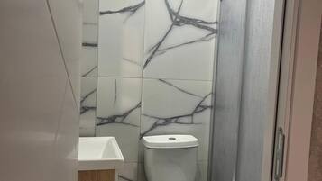 A bathroom with marble tiles, a toilet, a sink, and a shower.