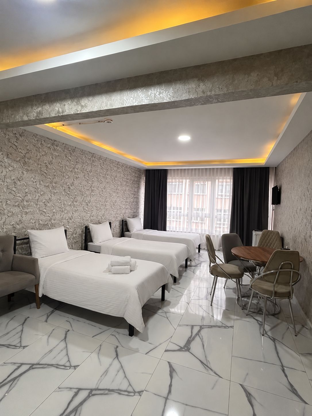 A hotel room with two beds, a dining table, and a TV.