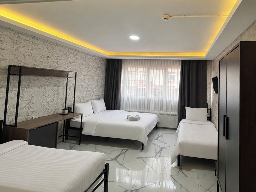 A hotel room with two beds, a desk, a wardrobe, and a large window with curtains.