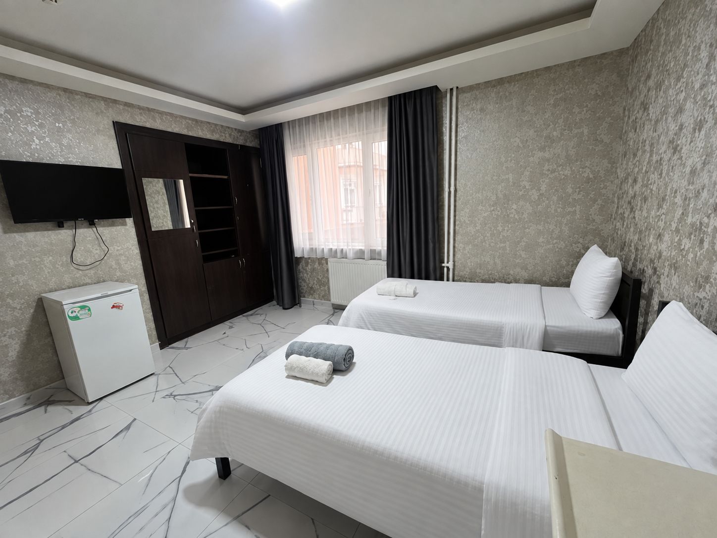 Une chambre d’hôtel avec deux lits, une armoire, une télévision et un petit réfrigérateur.