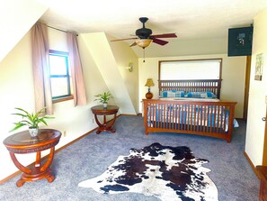 A room with a crib, a ceiling fan, a window with curtains, a small table with a plant, and a cowhide rug. - Flat Creek Overlook is a beautiful place to stay 20 min from roaring river! (Cassville)