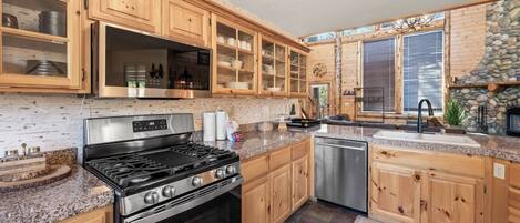 A kitchen with wooden cabinets, a stainless steel stove, granite countertops, and a stone fireplace.