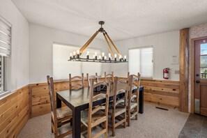 A wooden dining table with chairs, a hanging light fixture, and a fire extinguisher on the wall. - Timberline View Estate (Big Bear Lake)