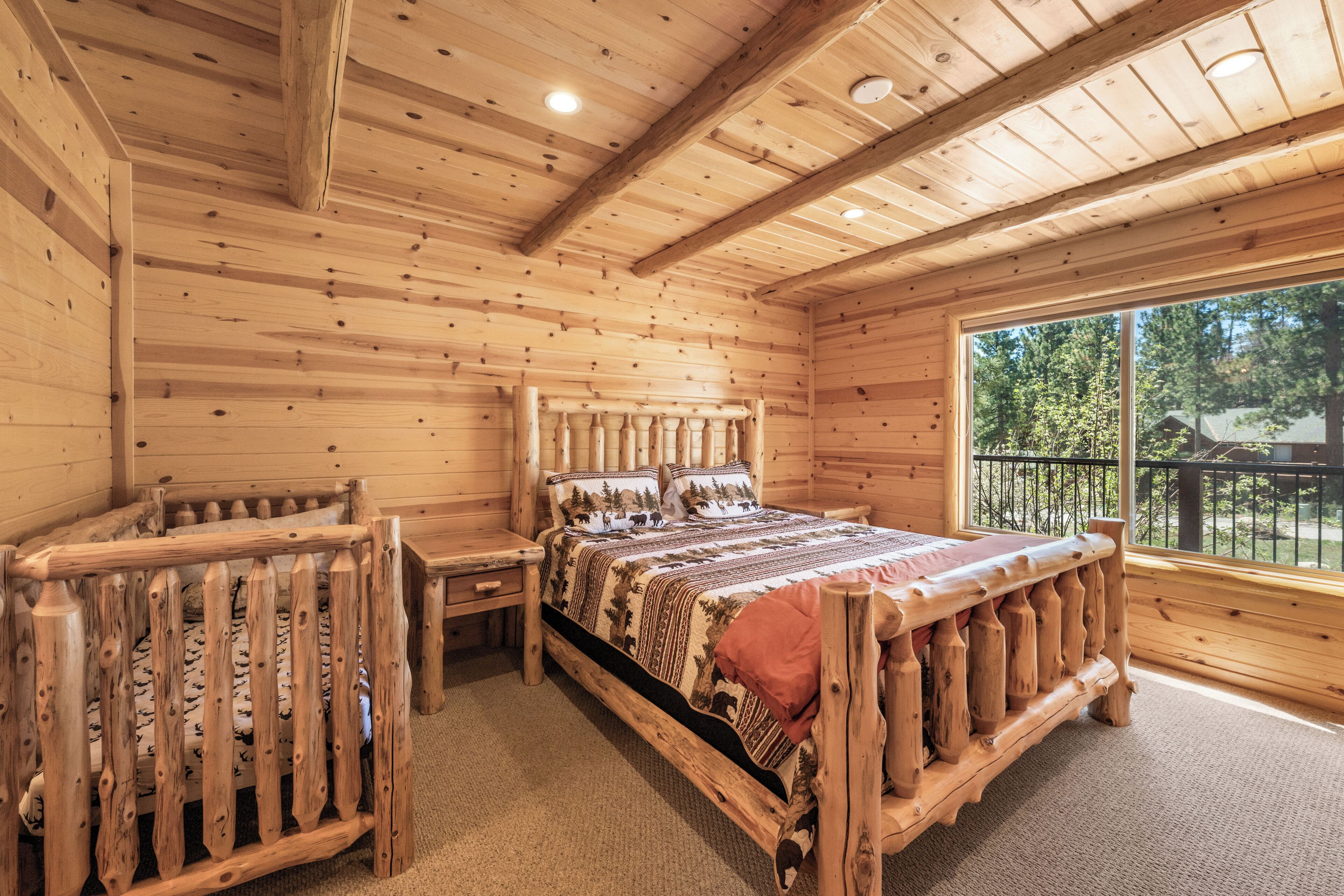Un dormitorio tipo cabaña de madera, con cama, mesita de noche y ventana con vistas a árboles.