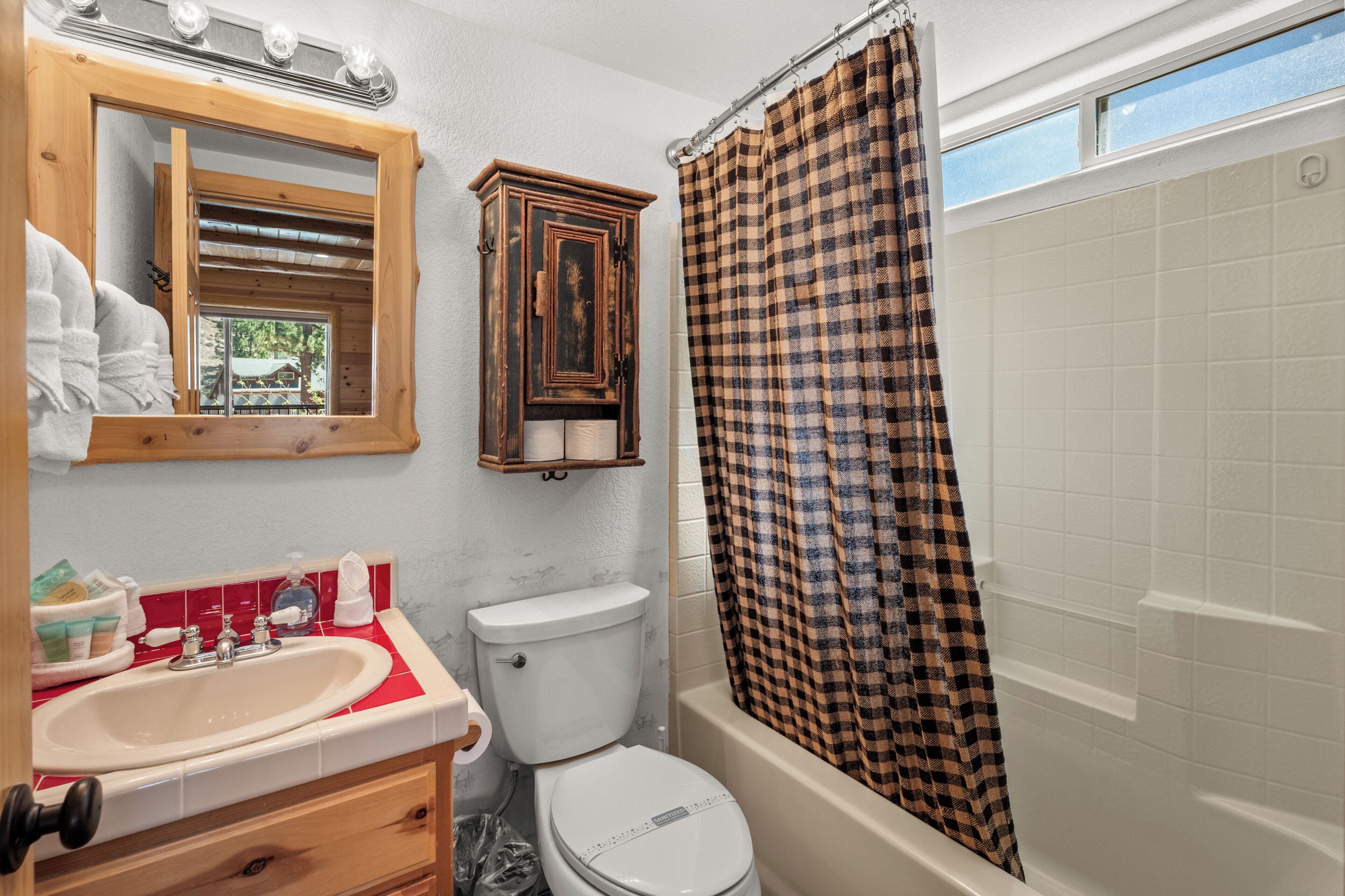 A bathroom with a sink, toilet, mirror, cabinet, and a checkered shower curtain.