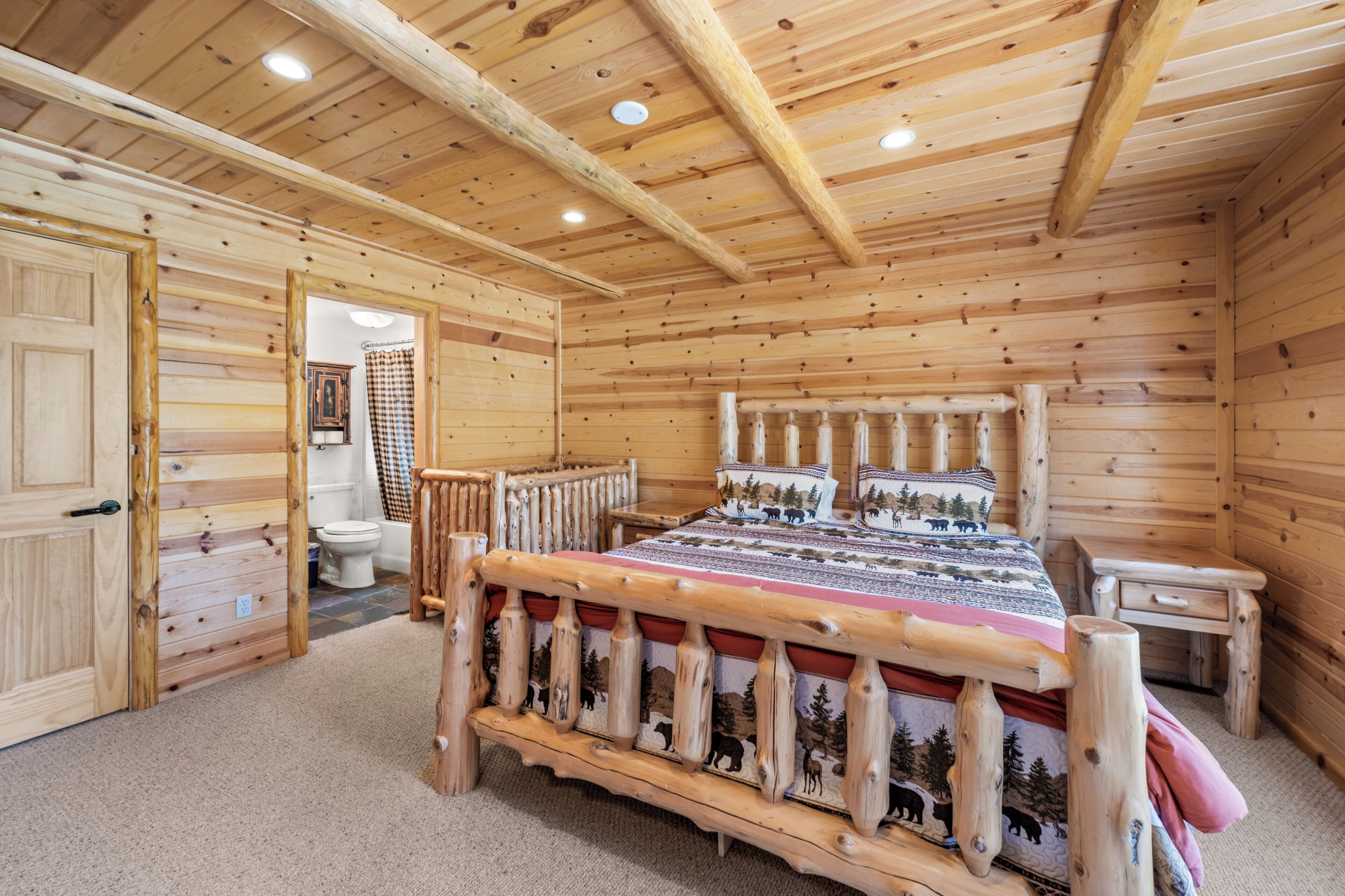 A wooden cabin interior with a bed, a bathroom, and a door leading to another room.