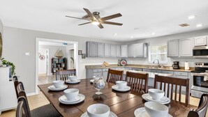Una cocina moderna con armarios grises, un comedor con mesa de madera dispuesta para cuatro, y un ventilador de techo.