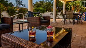 Un patio al aire libre con mobiliario de mimbre, una mesa de vidrio y dos bebidas.