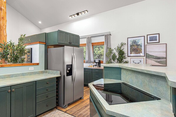 A modern kitchen with a built-in stove, stainless steel refrigerator, and green cabinetry. - Last Stand Pines is a charming cabin in Custer perfect for family getaways (Custer)