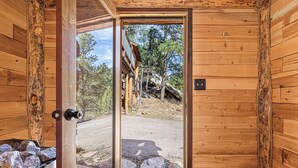 A wooden cabin with a door leading to an outdoor area with a view of trees and a building in the distance. - Last Stand Pines is a charming cabin in Custer perfect for family getaways (Custer)