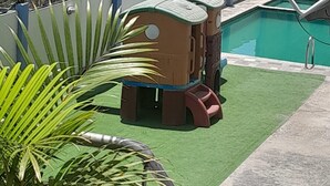 Ein Poolbereich mit Blick auf den Ozean, ein Gebäude im Hintergrund und eine Palme im Vordergrund.
