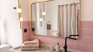 A bathroom with a marble sink, a large mirror, pink tiled walls, and a white radiator. - Casa Adamo- Rooftop Hideaway (Genova)