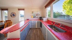 Una cocina compacta con encimera roja, un lavaplatos empotrado y un ventanal con vistas a zonas verdes.