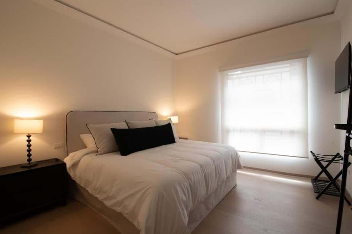 A bedroom with a bed, nightstands, a window, and a TV.