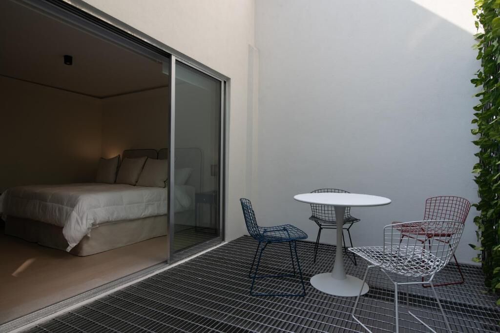 Un dormitorio con puerta corrediza de vidrio, una cama y un pequeño espacio exterior con mesa y sillas.