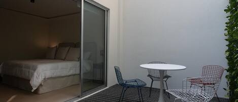 Un dormitorio con puerta corrediza de vidrio, una cama y un pequeño espacio exterior con mesa y sillas.