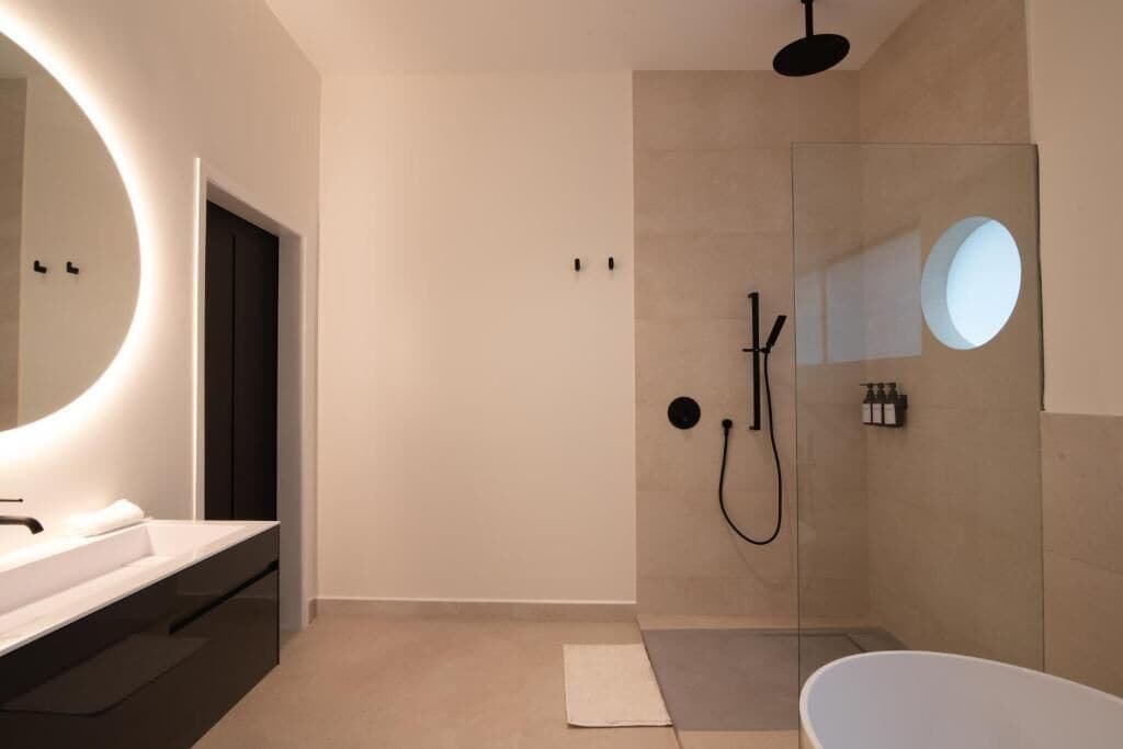 A modern bathroom with a large mirror, a bathtub, a shower area, and a vanity with a sink.