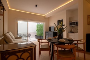Ein moderner Essbereich mit einem Tisch für vier Personen, einer Couch und Blick auf einen Balkon mit einer Grünpflanze.