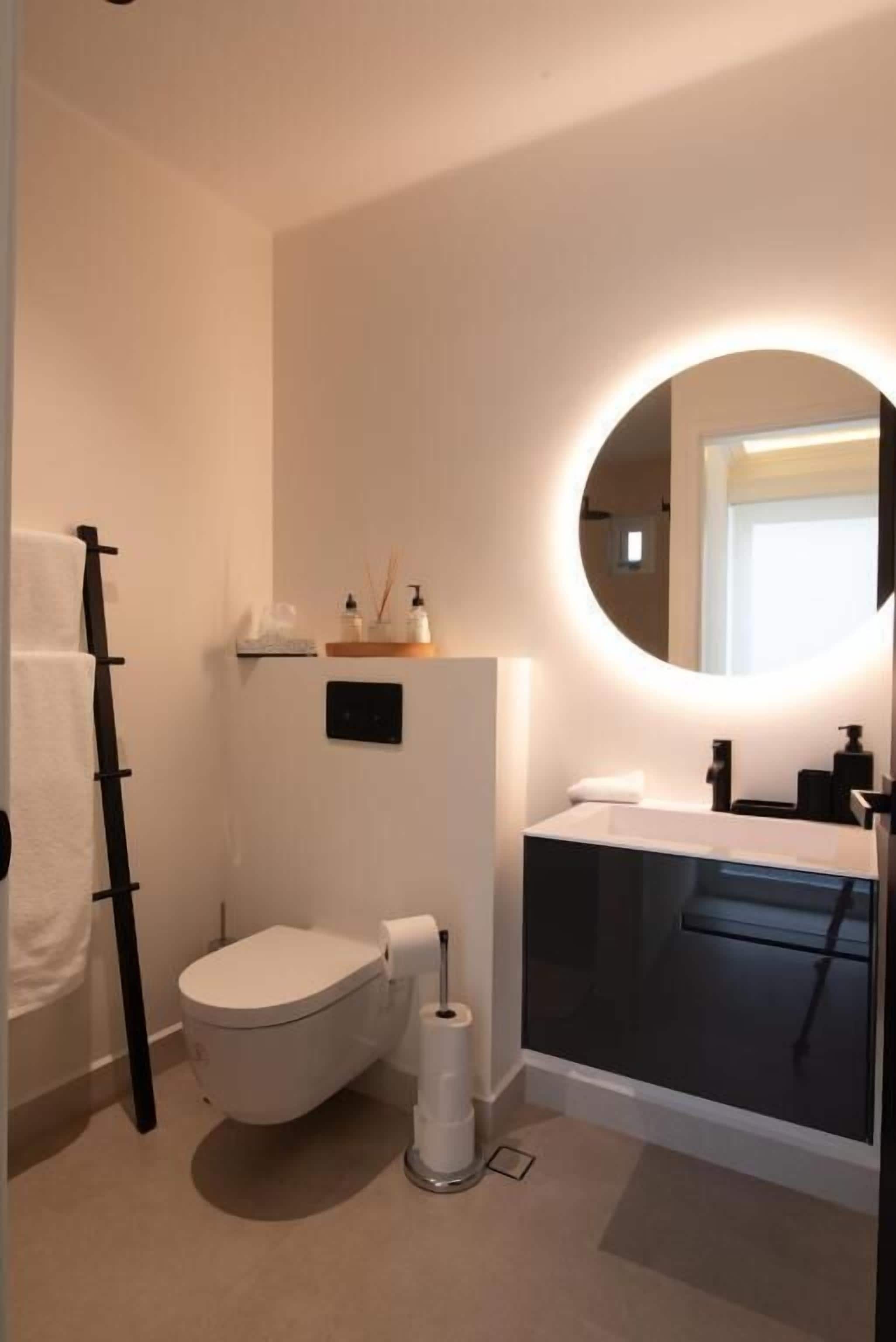 Un baño moderno con inodoro, lavamanos y espejo.