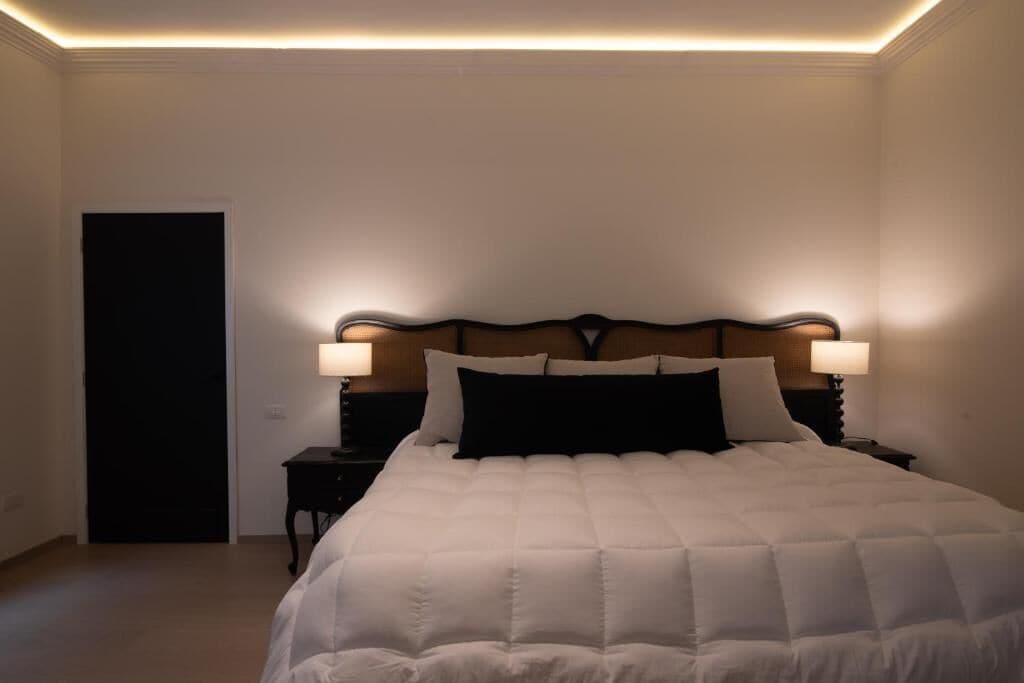 A bedroom with a large bed, two bedside tables with lamps, a door, and a ceiling light fixture.