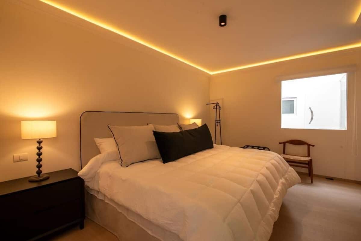A bedroom with a bed, bedside table, lamp, and a window.