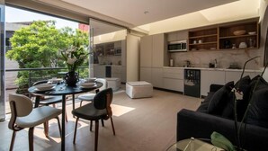 Eine moderne Küche mit integrierten Geräten, ein Essbereich mit Glastisch und ein Wohnbereich mit Sofa und Pflanze.