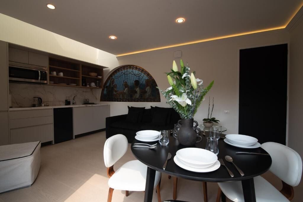 A modern kitchen with built-in appliances, a dining area with a black table and white chairs, and a decorative vase with flowers.