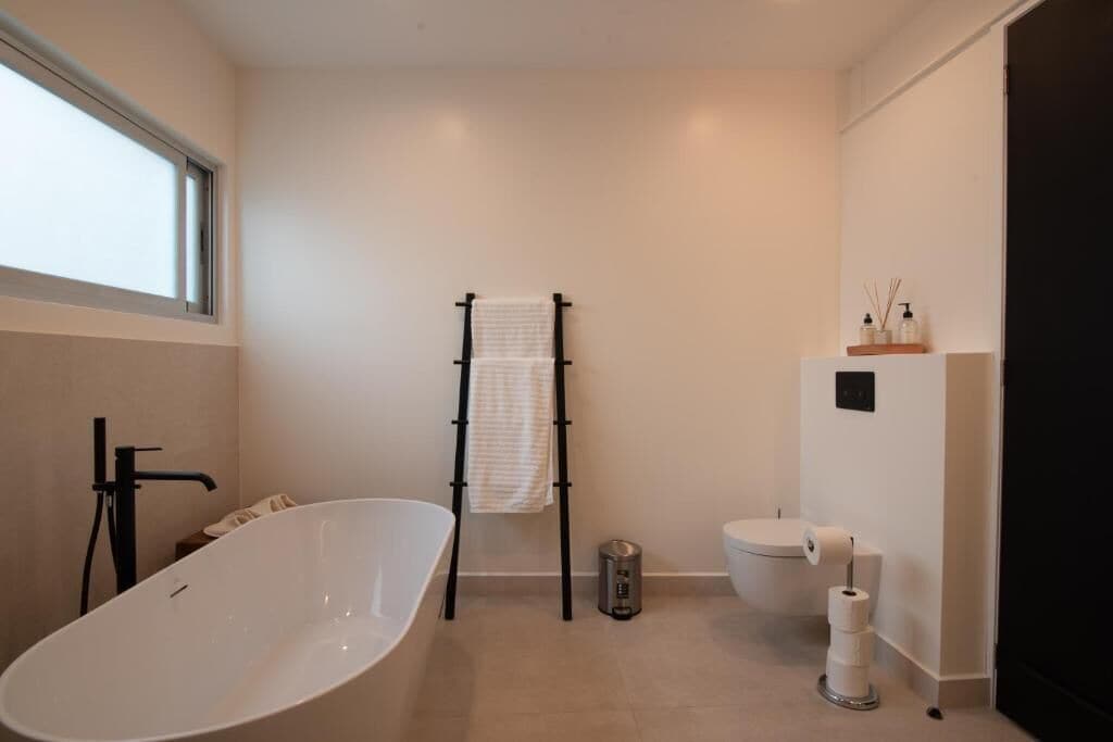 Et moderne badeværelse med et fristående badekar, et håndklædestativ, et toilet og et vindue.