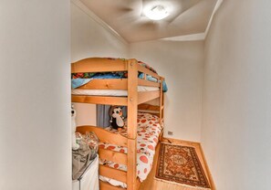 Ein Etagenbett mit einem Stofftier auf der unteren Liege, ein kleiner Tisch mit einem Glas und ein gemustertes Teppich auf dem Boden.